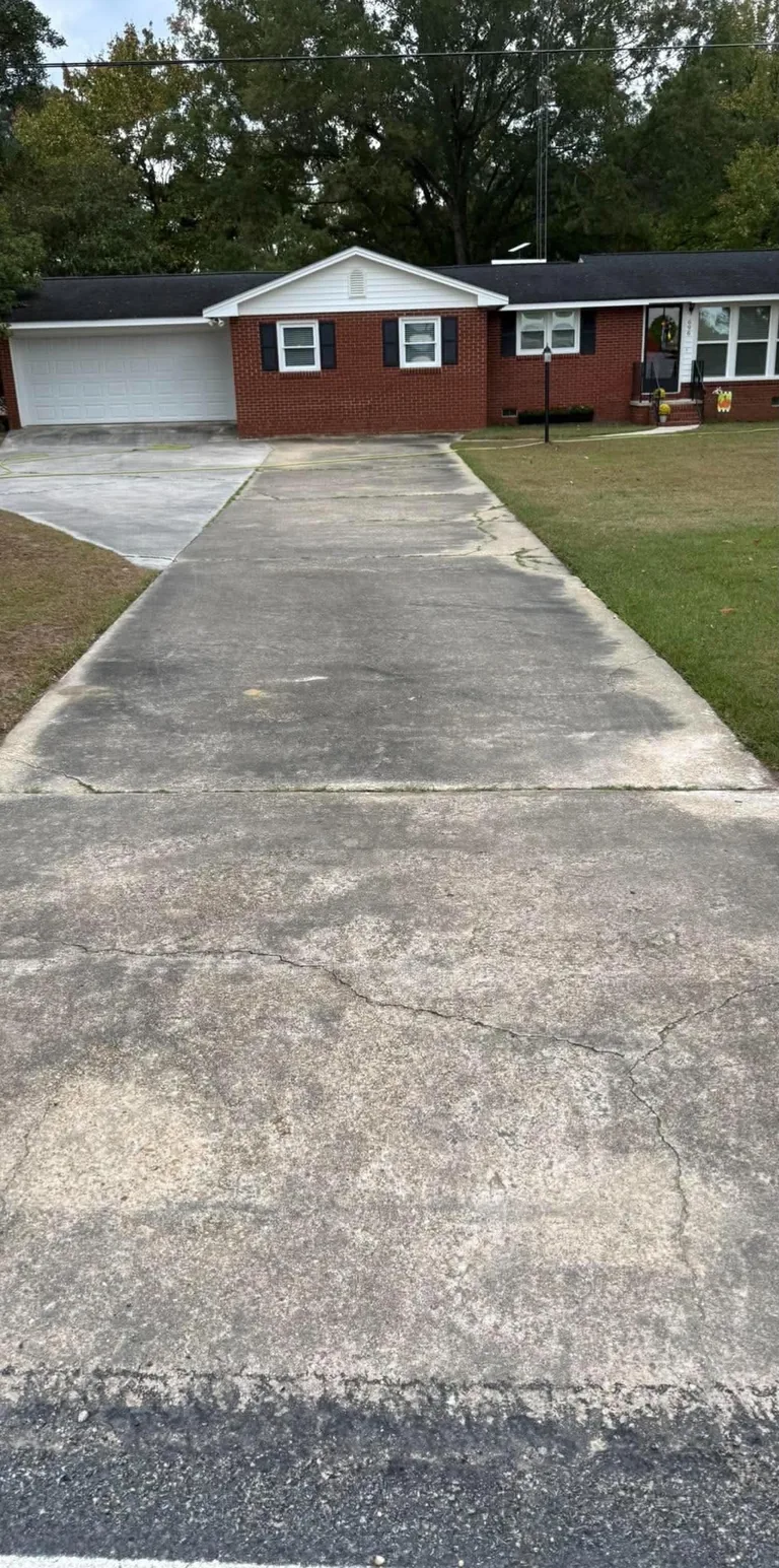 Dirty concrete driveway at a red brick ranch before cleaning